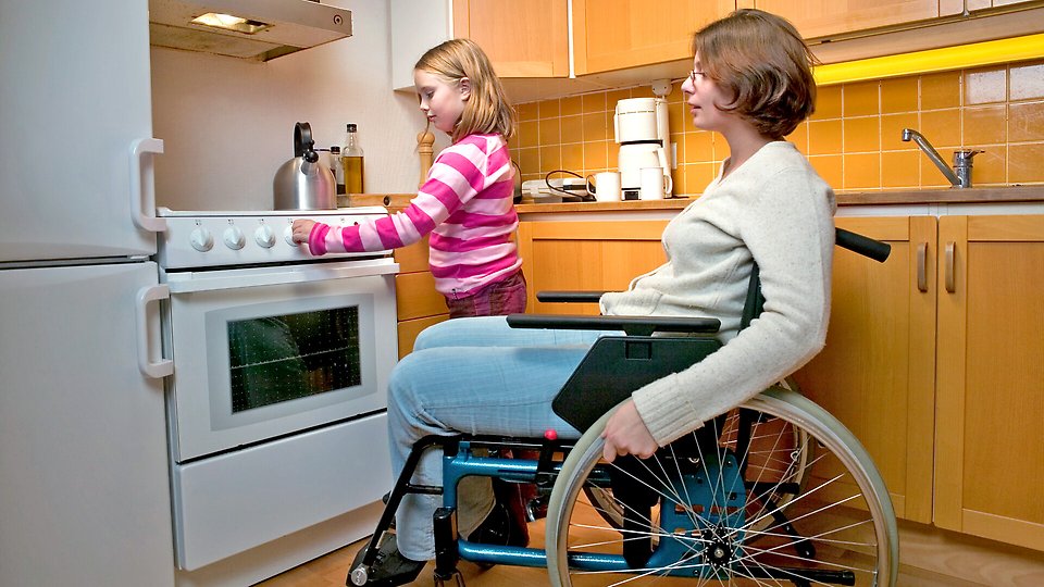En kvinna och en flicka i ett kök. Kvinnan sitter i rullstol.