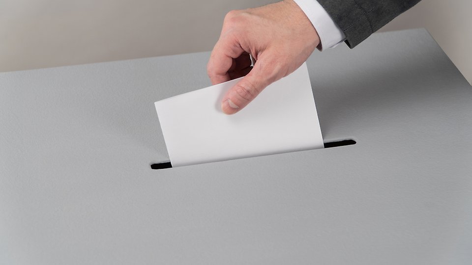 En manlig hand stoppar ner ett röstkort i en valurna