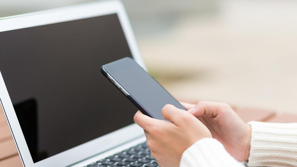 En kvinna håller i en mobiltelefon framför sin laptop