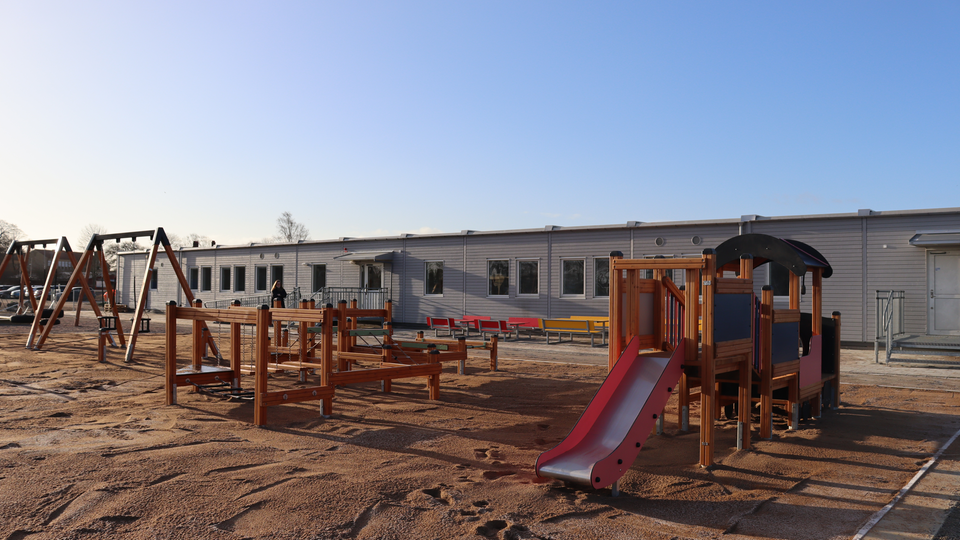 Lekplats i förgrunden och modulförskolan i bakgrunden